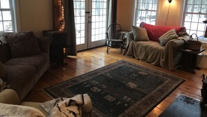 A cozy living room with a sofa, a chair, a rug, and a window with curtains. - Cozy cottage tucked away in the woods (Townshend)