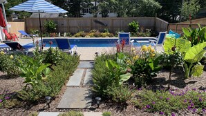 A backyard with a swimming pool, stone pathway, and various plants. - Pristine home w/heated saltwater pool, just minutes from beaches and bike trail. (Eastham)