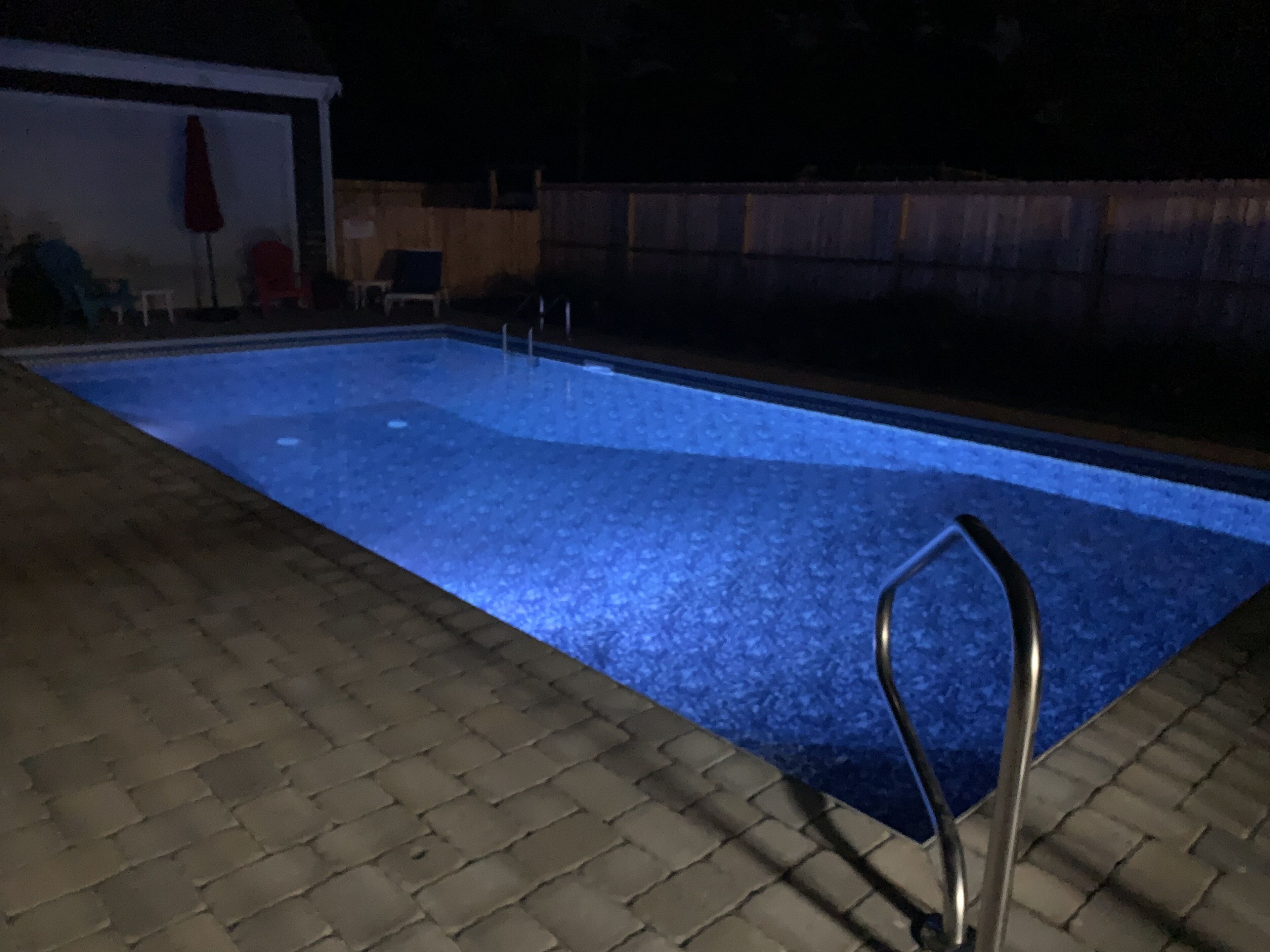 A rectangular swimming pool with a metal ladder on one side, surrounded by a brick patio.