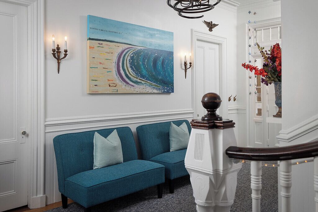 Ein Zimmer mit einem blauen Sofa, einem Gemälde, Wandleuchten und einer Treppe.