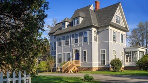 A two-story house with a front porch, a chimney, and a small attached garage. - King with Kitchenette and Fireplace, Private Bath, Parking, Walk to all (Newport)