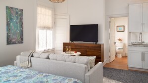 Moderni, hyvin valaistu huone, jossa on suuri sänky, televisio ja pieni keittiö.