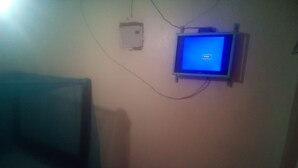 A room with a bed, a small table, a wall-mounted TV, and a power outlet. - Sky Guest House (Nairobi)