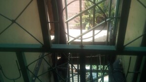 A view through a window with metal bars, a bicycle, and a building with a red roof in the background. - Sky Guest House (Nairobi)