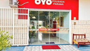 A hotel entrance with a red and white facade, a glass door, and a small outdoor seating area. - OYO Pousada Paraná, Cuiabá (Cuiabá)