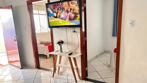 A hotel lobby with a tiled floor, a television mounted on the wall, a small wooden table with a vase, and a red and white chair. - OYO Pousada Paraná, Cuiabá (Cuiabá)