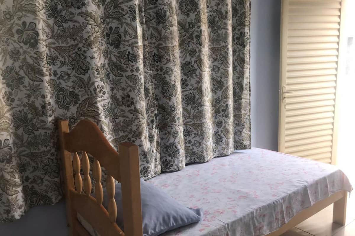 A single bed with a wooden headboard, a floral-patterned bedspread, and a window with a floral curtain.