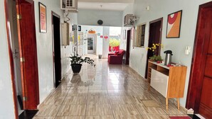 A hallway with a tiled floor, a potted plant, a red chair, and a small wooden table with a kettle. - OYO Pousada Paraná, Cuiabá (Cuiabá)