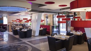 Un restaurante moderno con mesas redondas, lámparas colgantes rojas y un elemento decorativo en el suelo.
