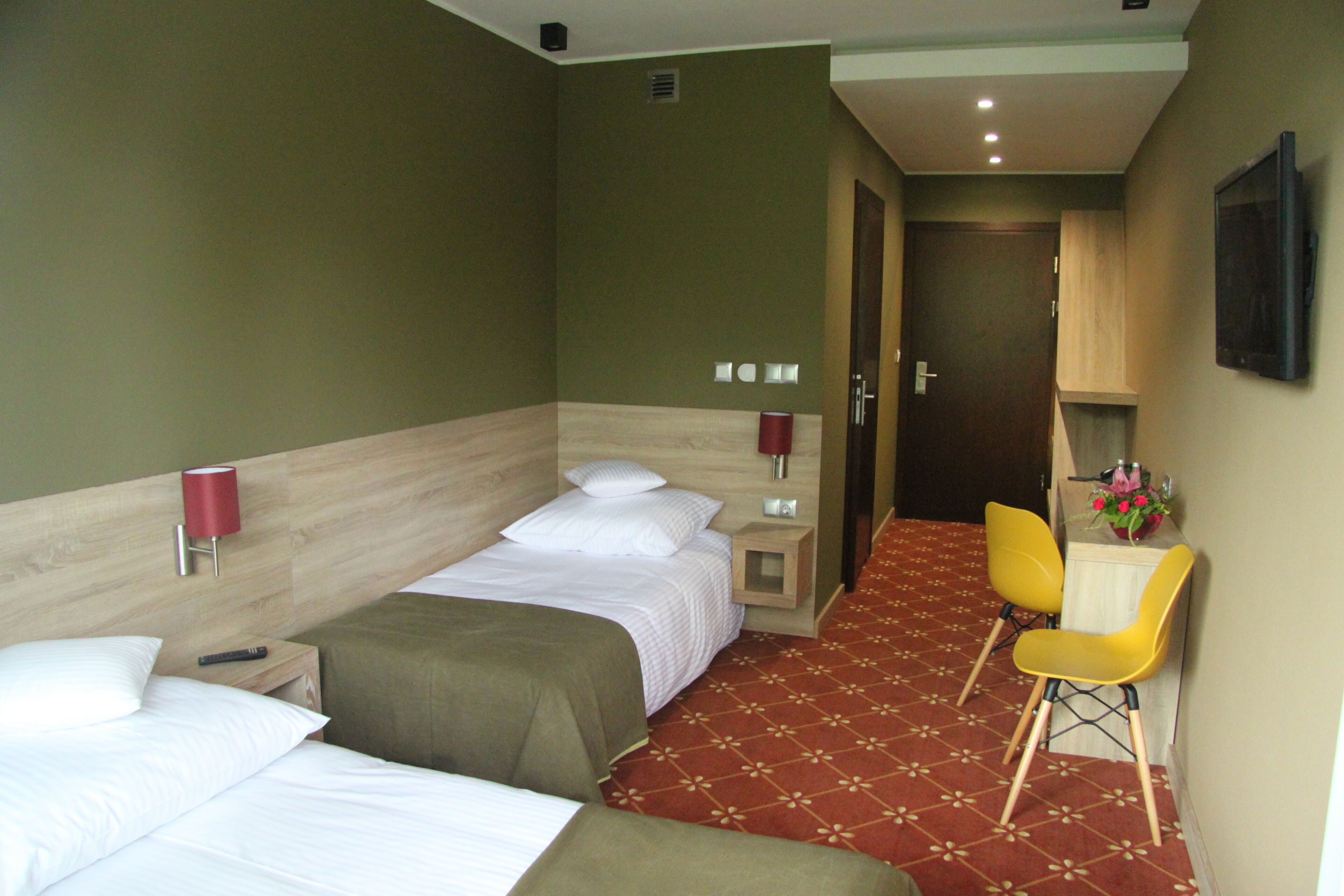 Habitación de hotel con dos camas, un escritorio con silla, televisor y una mesita con un florero.