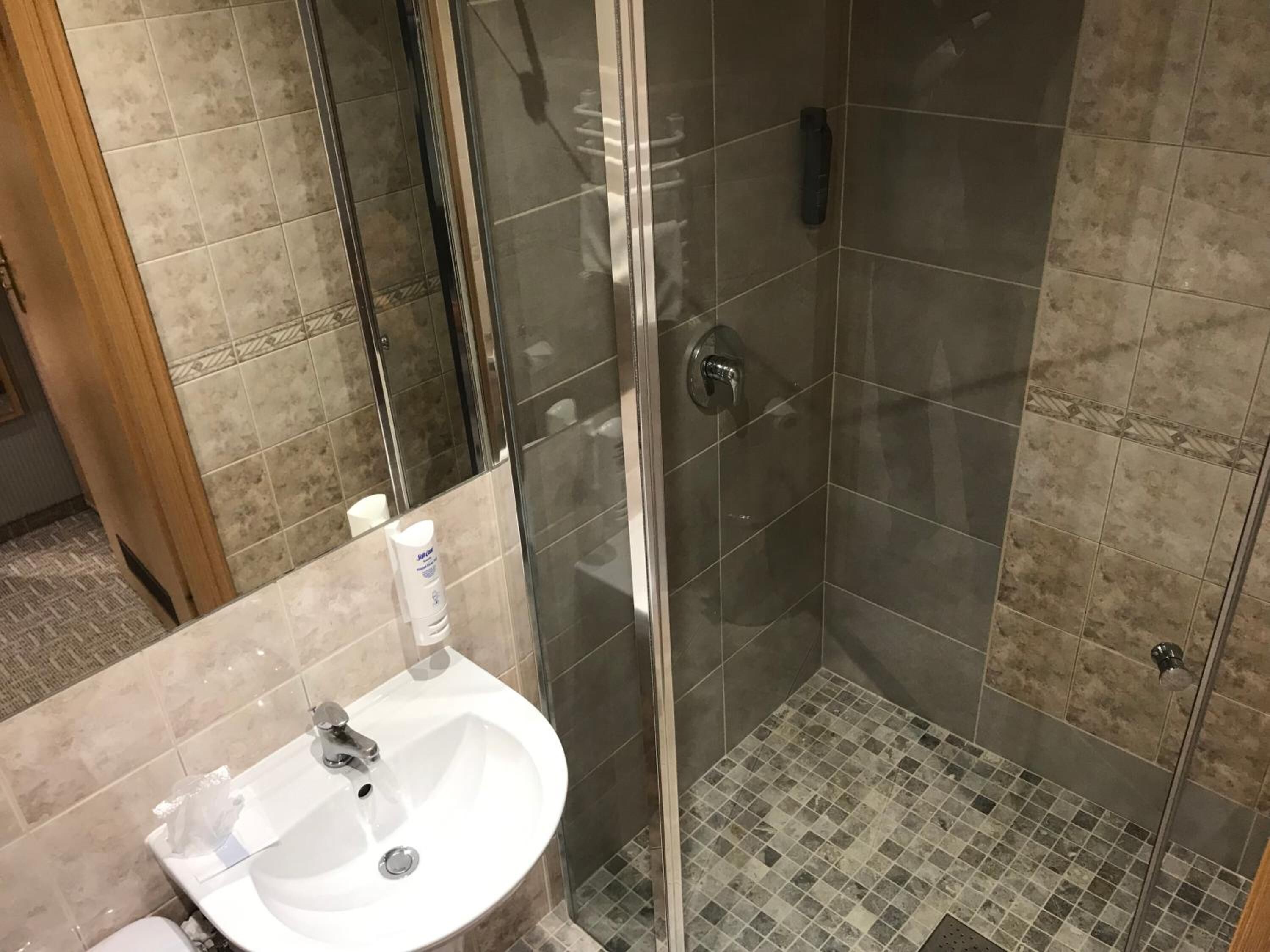 Et badeværelse med et glasafskærmet brusebad, en håndvask med spejl og fliserede vægge.