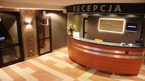 Zona de recepción de un hotel con un mostrador curvo, un reloj y un letrero que dice 'RECEPTORY HOTEL DUNAJEC'.