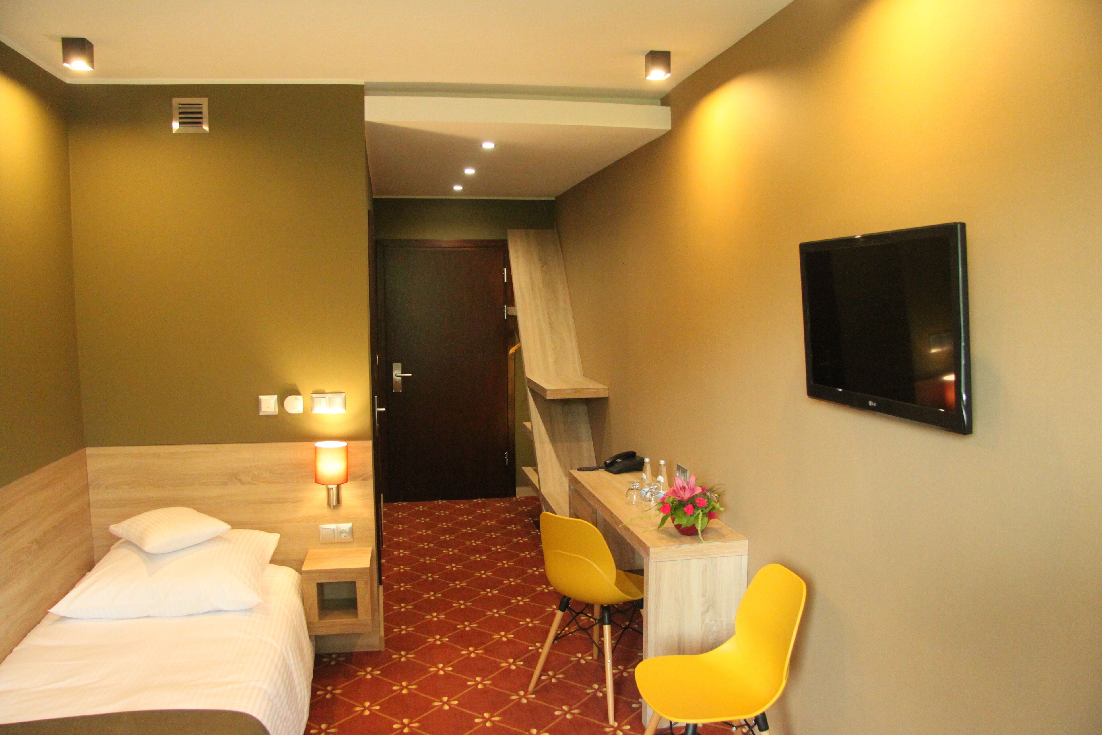 Ein Hotelzimmer mit einem Bett, einem Schreibtisch mit Stuhl, einem Fernseher und einem kleinen Tisch mit Blumenvase.
