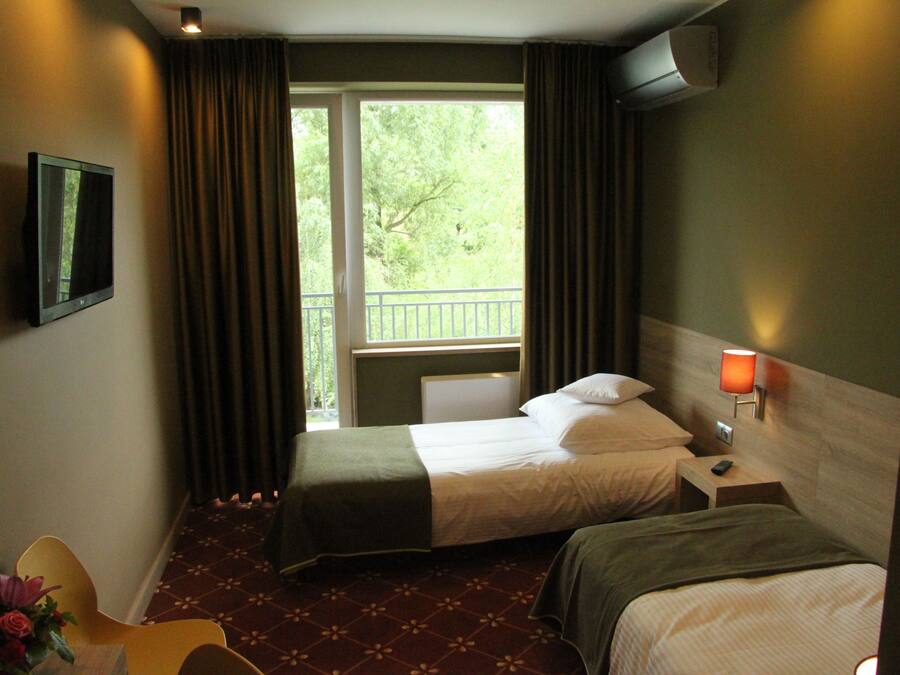 Habitación de hotel con dos camas, televisión, mesita de noche con lámpara y vistas a zonas verdes.