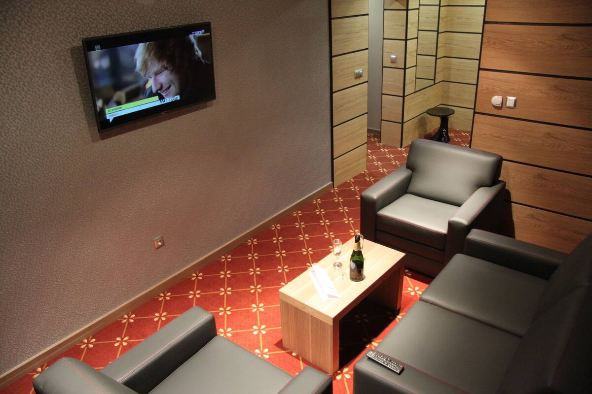 Un salón de cine con un televisor de pantalla plana montado en la pared, una mesa de centro de madera con una botella y un vaso, y asientos de cuero.
