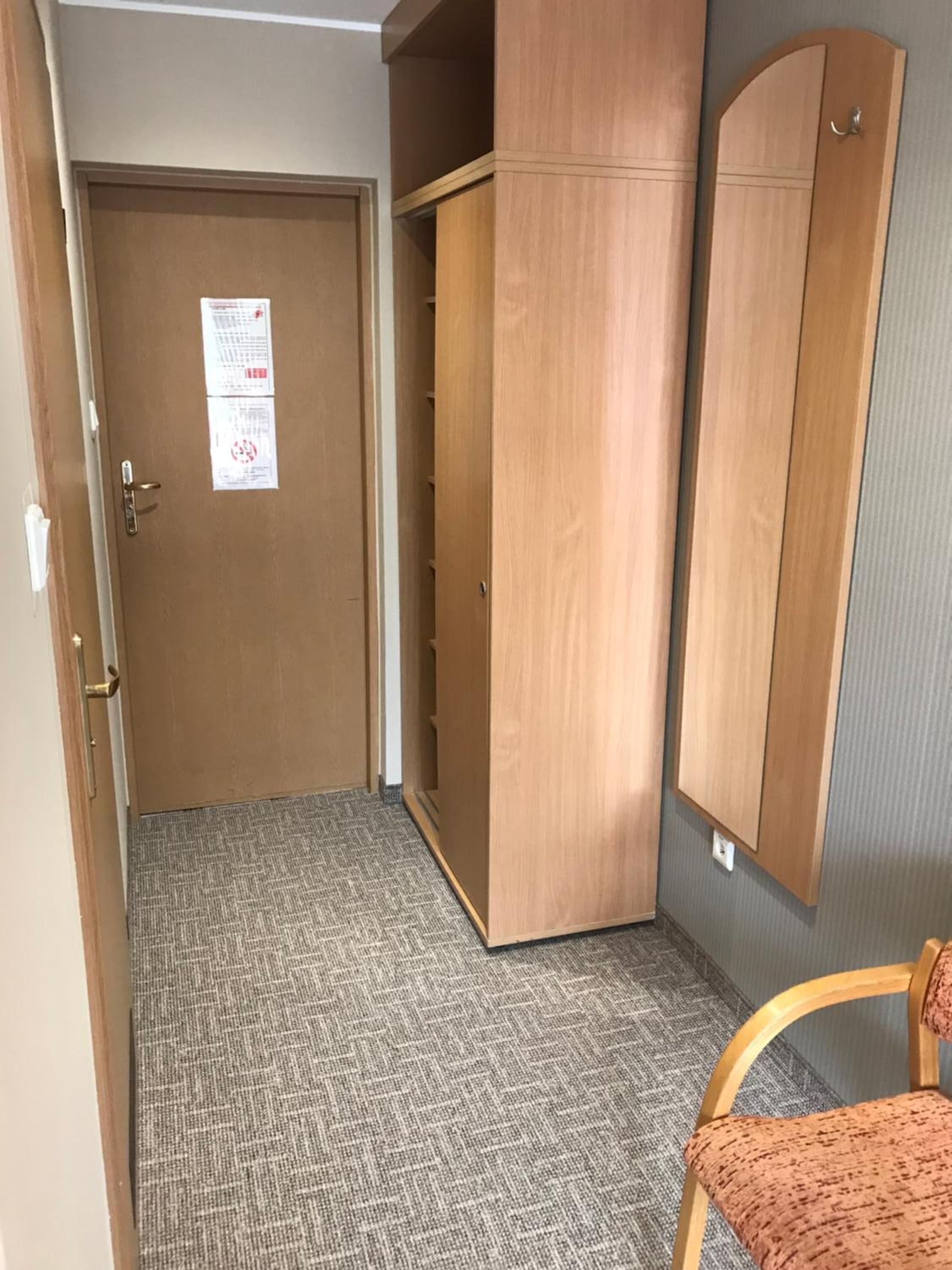 Una habitación con una puerta marrón, un armario de madera y una alfombra estampada.