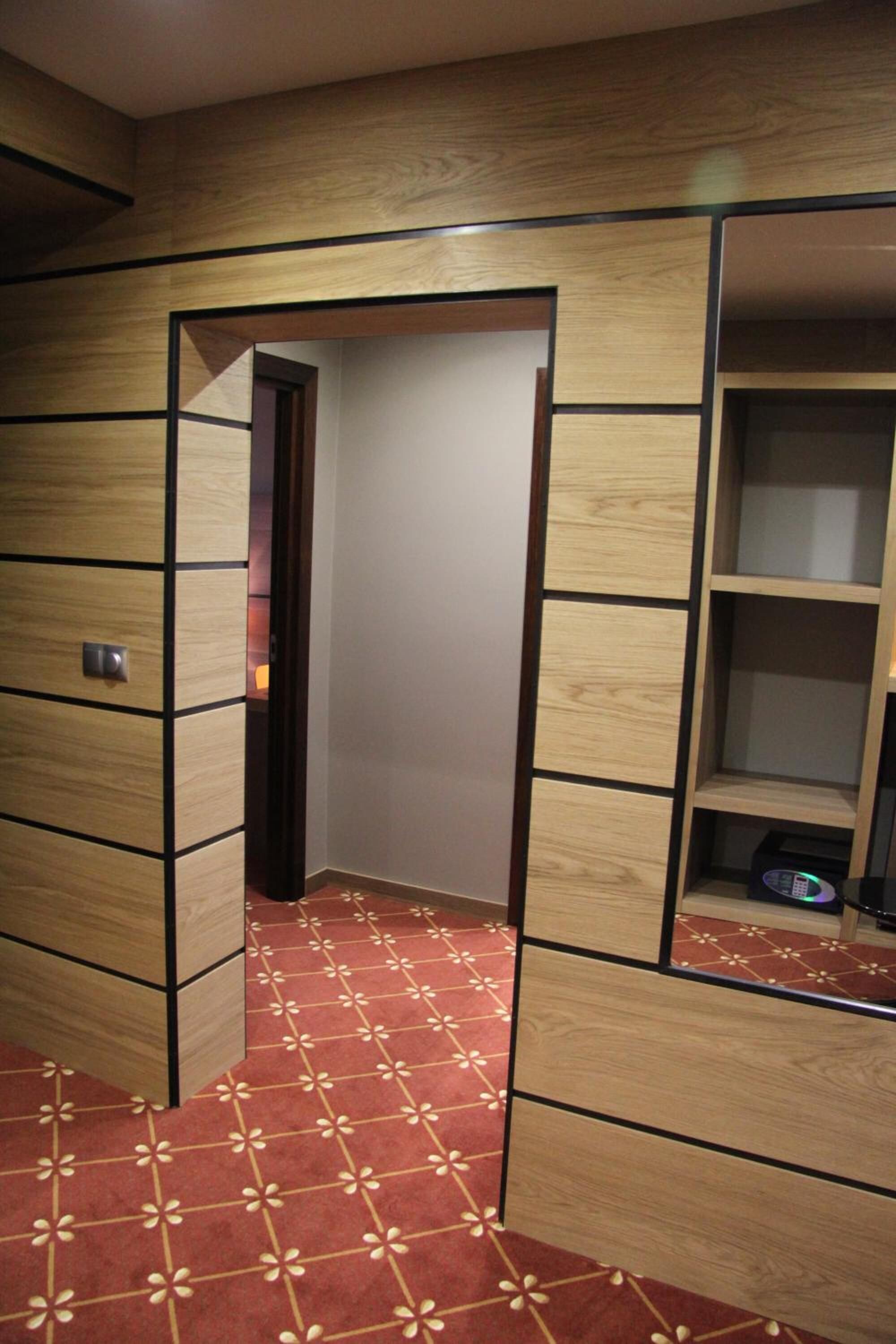 Habitación de hotel con un armario de madera, una alfombra roja estampada y un pequeño estante con un control remoto.