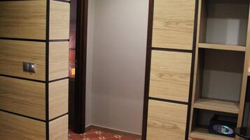 Habitación de hotel con un armario de madera, una alfombra roja estampada y un pequeño estante con un control remoto.