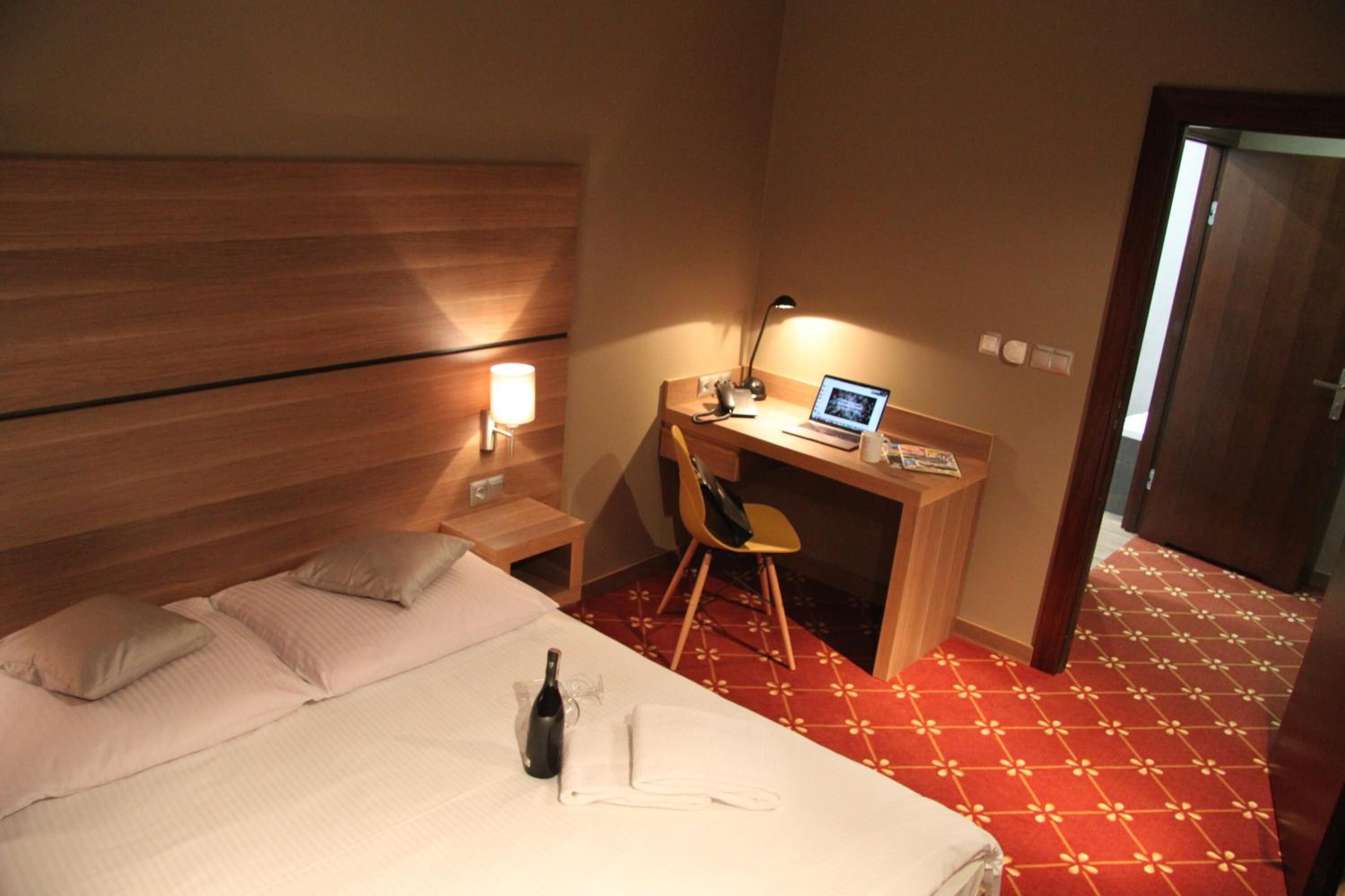 Une chambre d’hôtel avec un lit, un bureau avec un ordinateur portable, une chaise et une bouteille posée sur le lit.