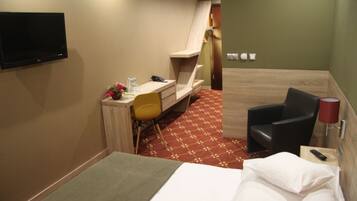 A hotel room with a bed, a desk, a chair, a TV, and a lamp.