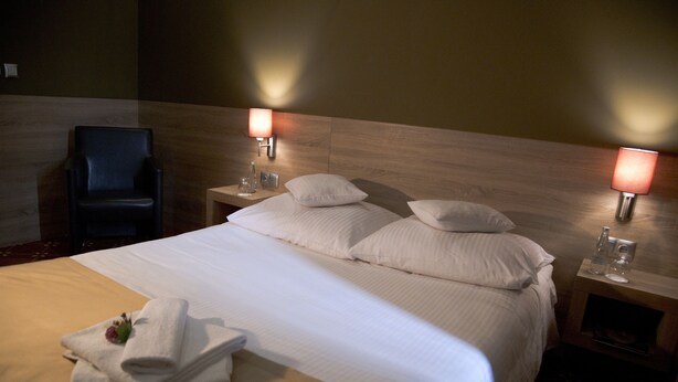Una habitación de hotel con una cama grande, dos mesitas de noche, una silla y lámparas de pared.