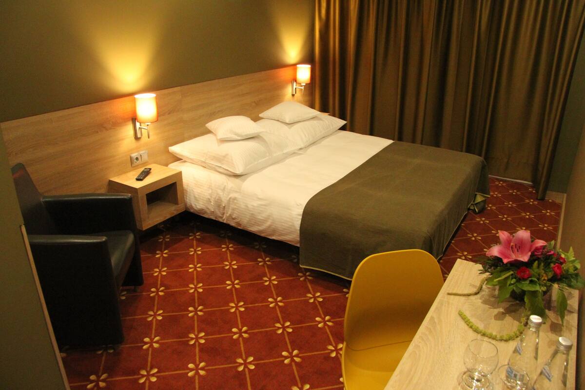 Habitación de hotel con cama, mesita de noche, lámpara, silla y una mesa con un jarrón de flores.