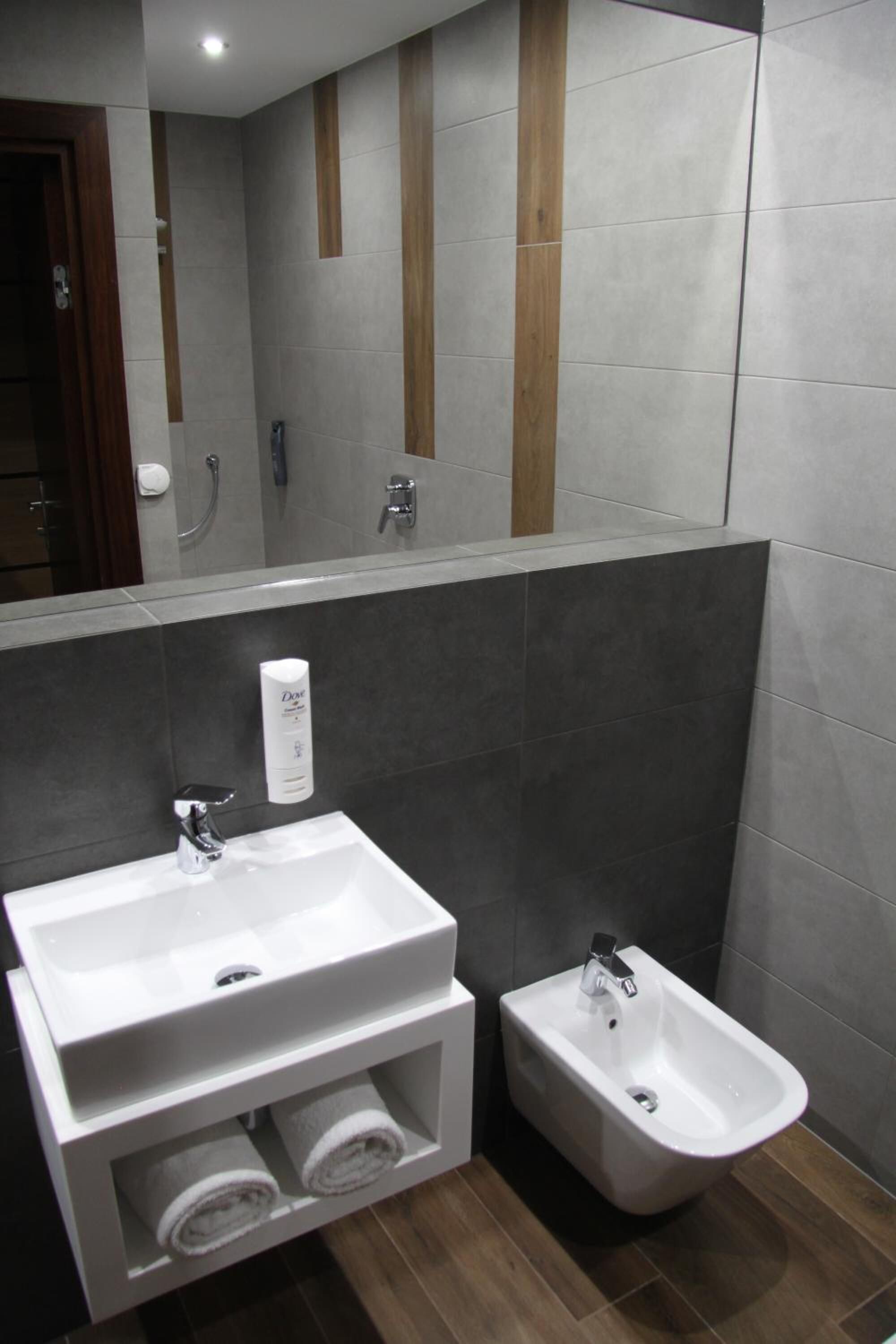 Ein modernes Badezimmer mit einem großen Spiegel, einem weißen Waschbecken, einem Bidet und einem Handtuchhalter.