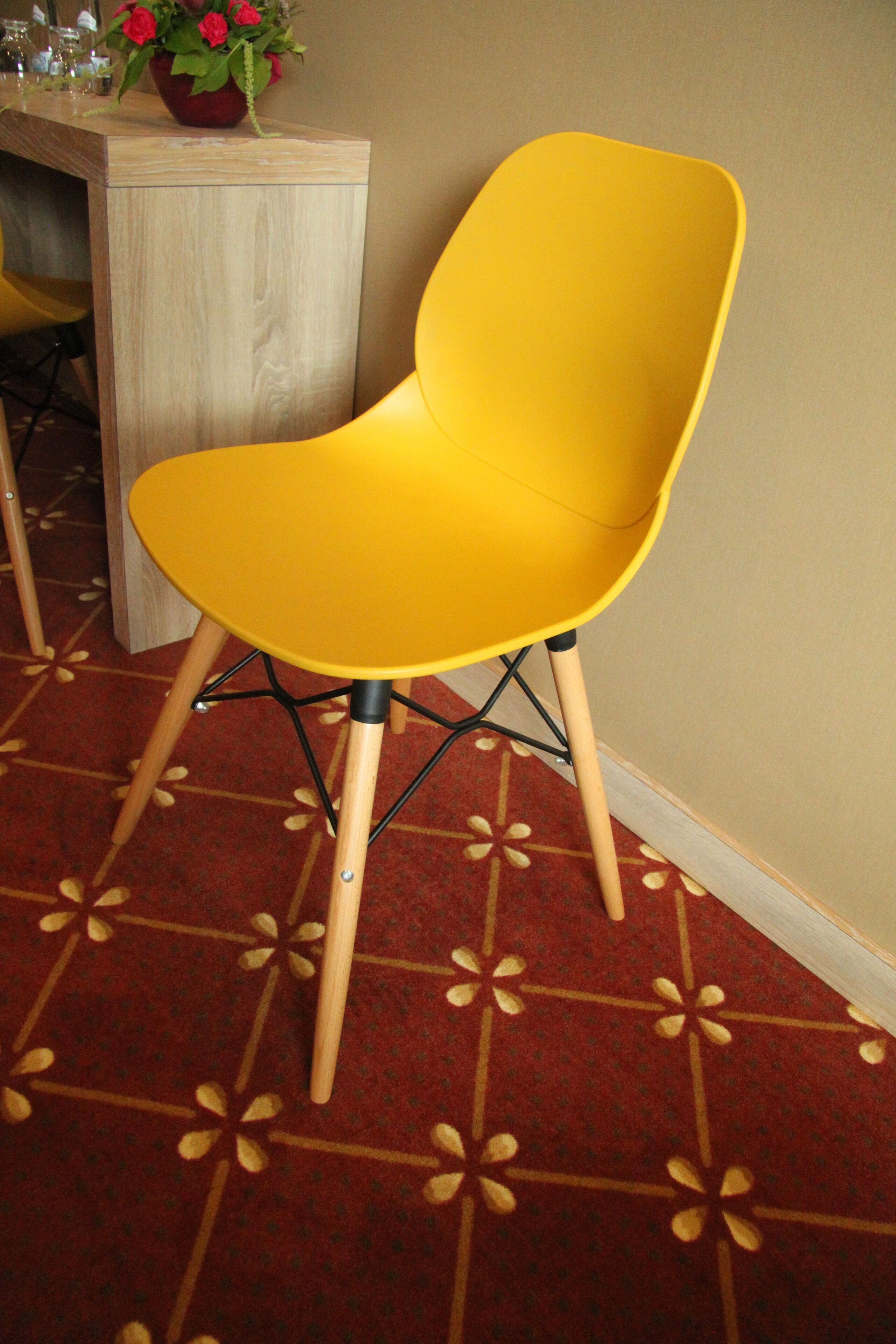Una silla amarilla con patas de madera y estructura de metal negro, sobre una alfombra estampada.