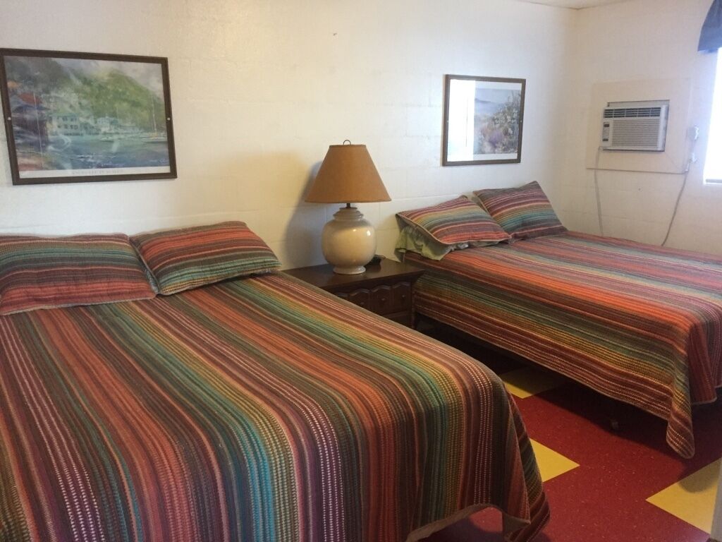 Una habitación con dos camas, cada una con ropa de cama a rayas, una lámpara de noche y cuadros en las paredes.