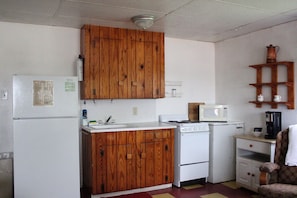 A compact kitchen with wooden cabinets, a refrigerator, a microwave, a stove, and a small cabinet with a coffee maker. - The Rocks: Fire Pit & Queen Beds Cozy Family Suite (Kingsland)