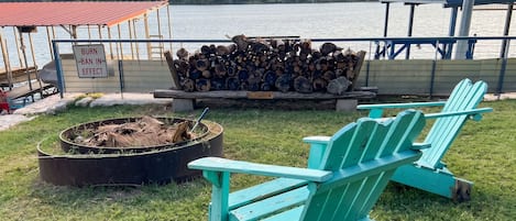 Un área de estar al aire libre junto al lago, con una chimenea, un montón de leña y un cartel que indica prohibición de incendios.