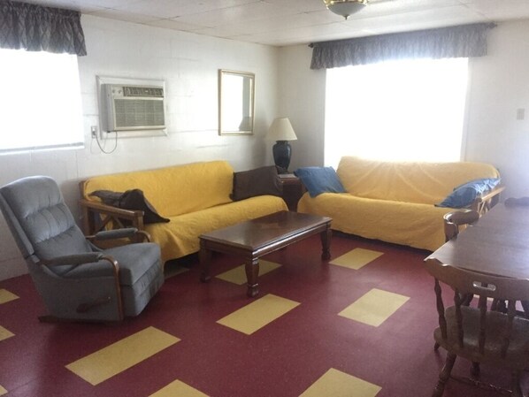 A living room with two yellow sofas, a wooden coffee table, a grey armchair, and a wooden dining table. - Lakefront Suite - 12 (Kingsland)