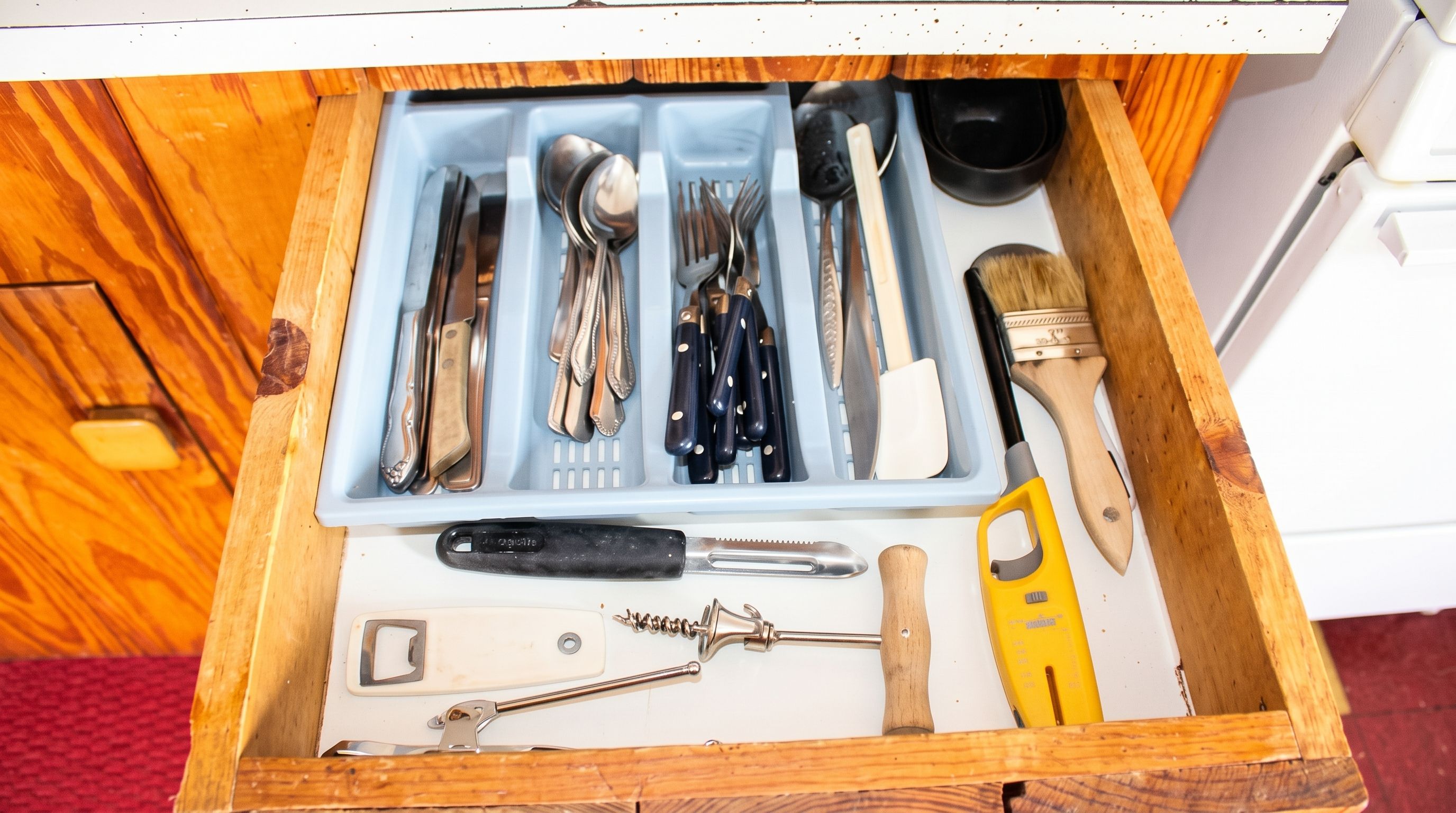 A drawer with various kitchen utensils and tools, including knives, spoons, and a measuring cup.
