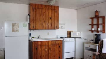A compact kitchen with wooden cabinets, a refrigerator, a microwave, and a stove.