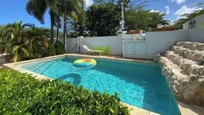 Una piscina con agua cristalina azul, rodeada de vegetación y un muro blanco.
