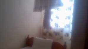 A bedroom with a bed, a window with curtains, and a hanging light fixture. - Club Dee Hotel (Kagio)