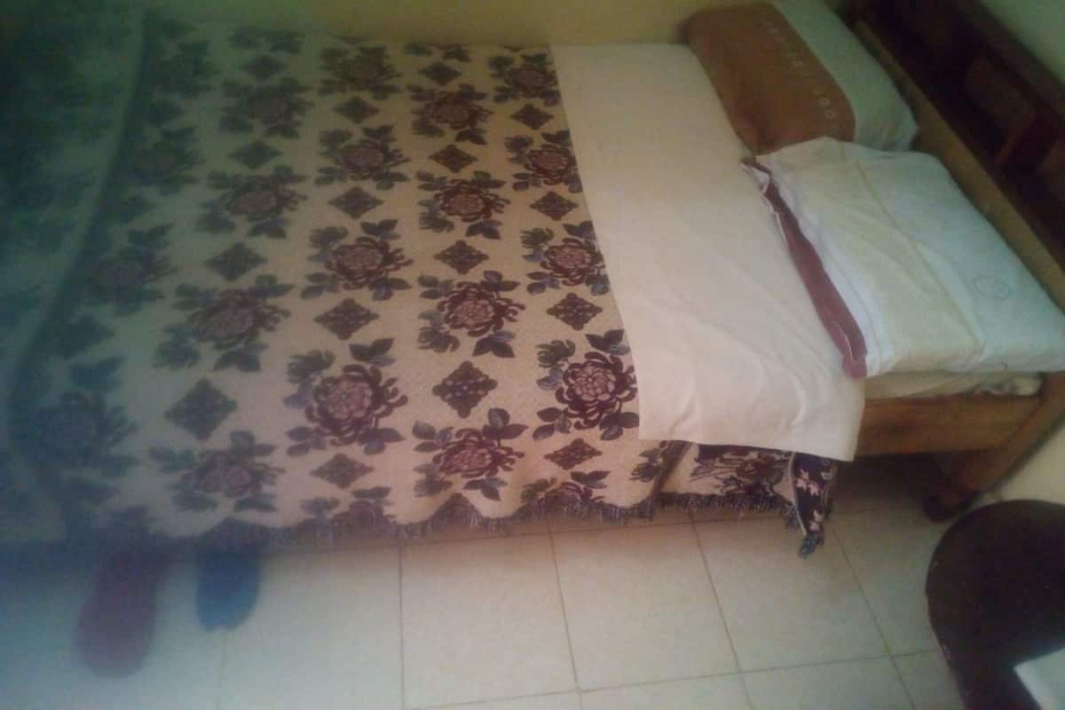 Uma cama com colcha florida, cabeceira de madeira e travesseiro branco.