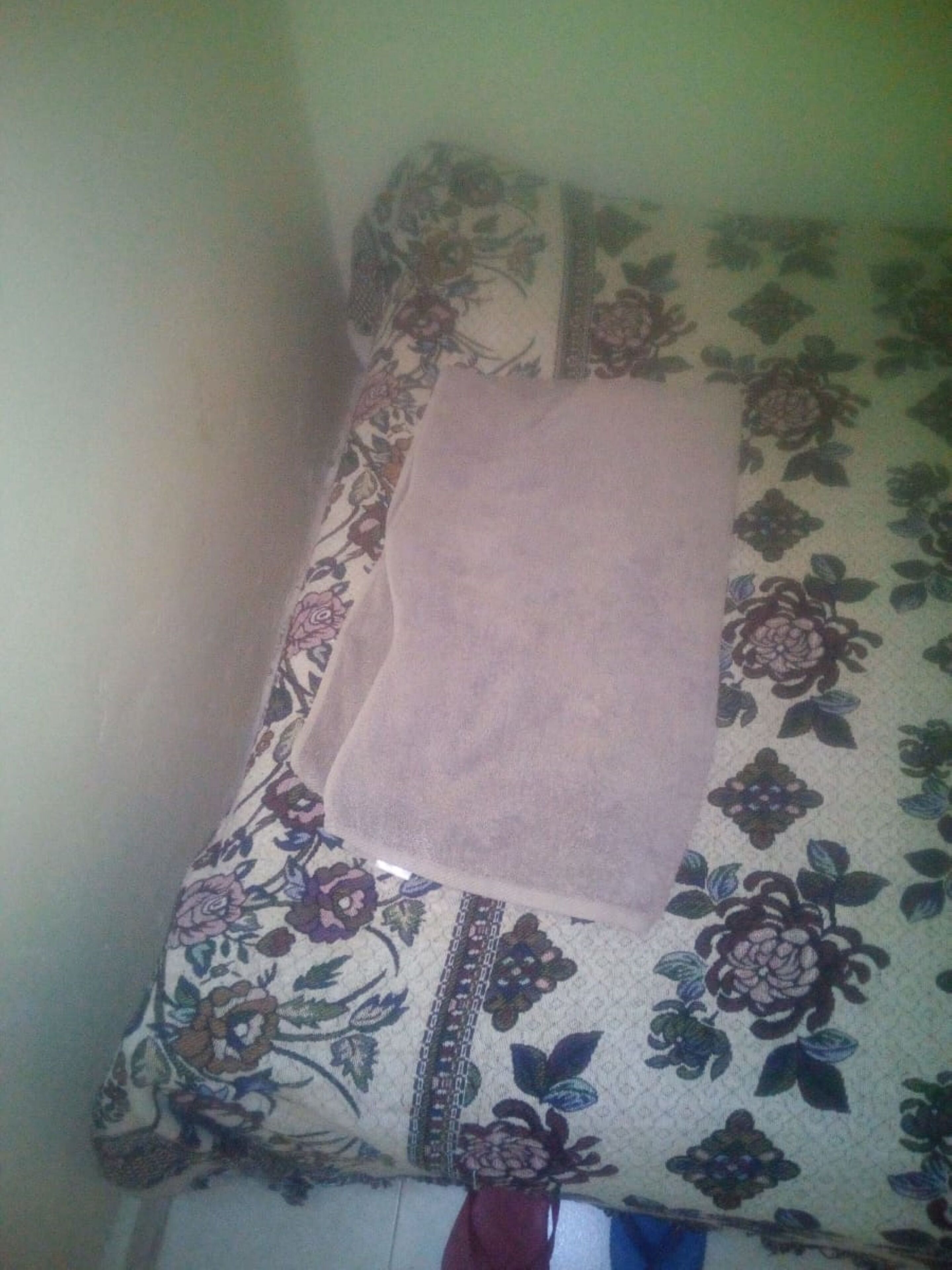 A bed with a floral-patterned bedspread and a pink blanket.