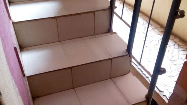 Unos escalones de baldosas color beige con barandilla metálica, que conducen a un espacio exterior con piso de baldosas.