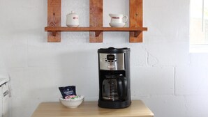 Una cafetera sobre una mesa, con un tazón de cápsulas de café y un sobre de crema.