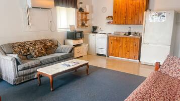Un espace de vie compact comprenant un canapé, une table basse, une kitchenette avec des meubles en bois, un réfrigérateur et un téléviseur.