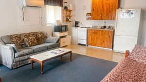 A compact living space with a sofa, a coffee table, a kitchenette with wooden cabinets, a refrigerator, and a television. - Kingsland Pet Friendly Long Term Suite Sleeps 8 (Kingsland)