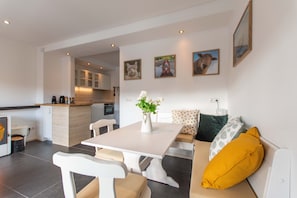 A modern kitchen with white cabinets, a dining area with a white table and chairs, and a sofa with patterned cushions.
