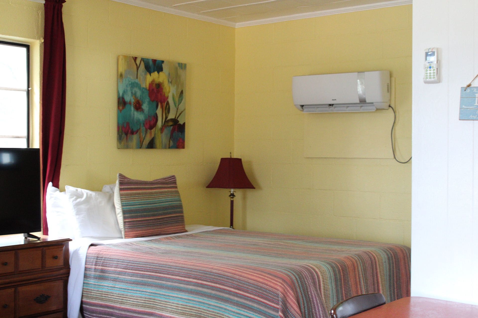 Et hotelværelse med seng, fjernsyn, et billede, en aircondition og en telefon.