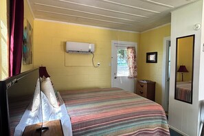 A room with a bed, a bedside table, a mirror, a door, and an air conditioning unit. - ﻿﻿Pet‑Friendly Lakefront Cabin, Winter Texan Stay (Kingsland)