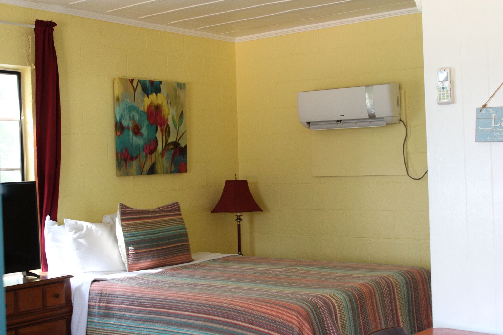 Una habitación con una cama, aire acondicionado de pared, un cuadro y una lámpara.