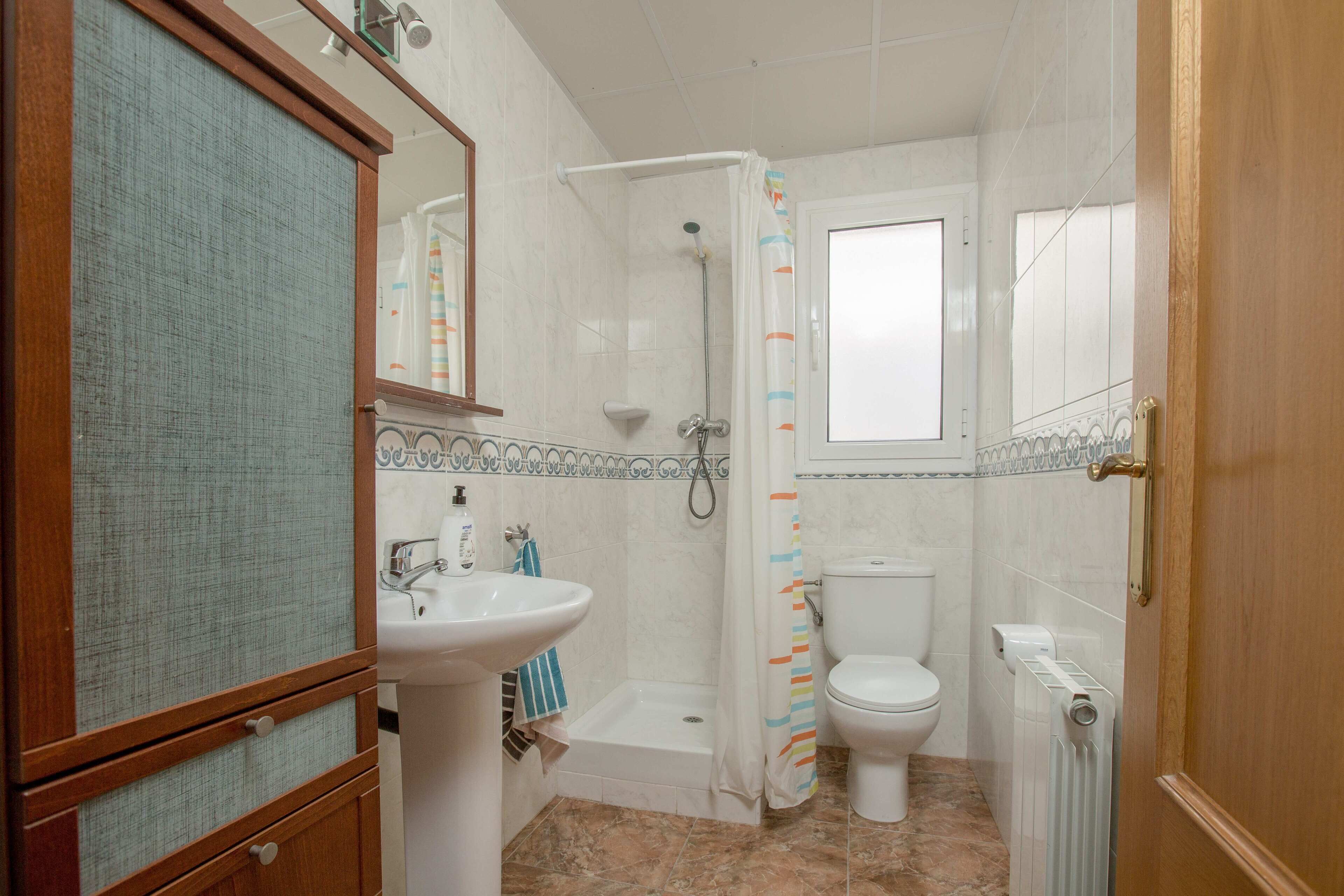 A bathroom with a sink, toilet, shower, and a wooden cabinet.