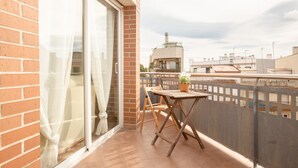 Ein Balkon mit Tisch und Stühlen, einem Blumentopf und Blick auf Gebäude im Hintergrund.