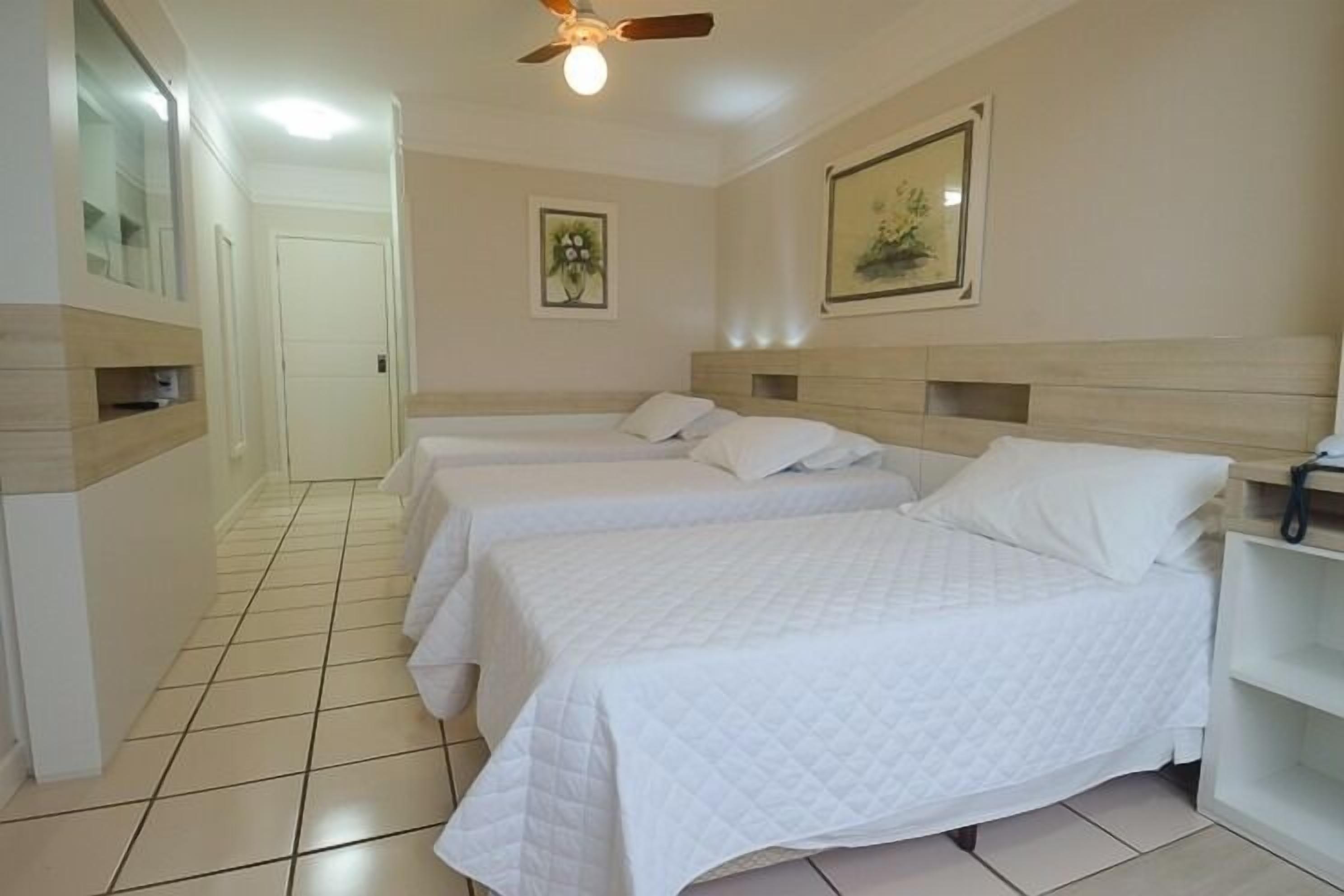 A hotel room with two beds, a ceiling fan, and a framed picture on the wall.