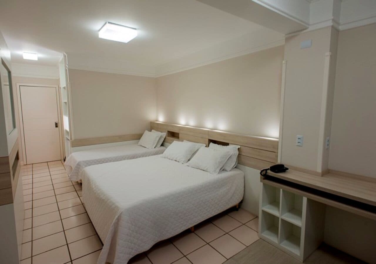 A hotel room with two beds, a desk, and a chair.